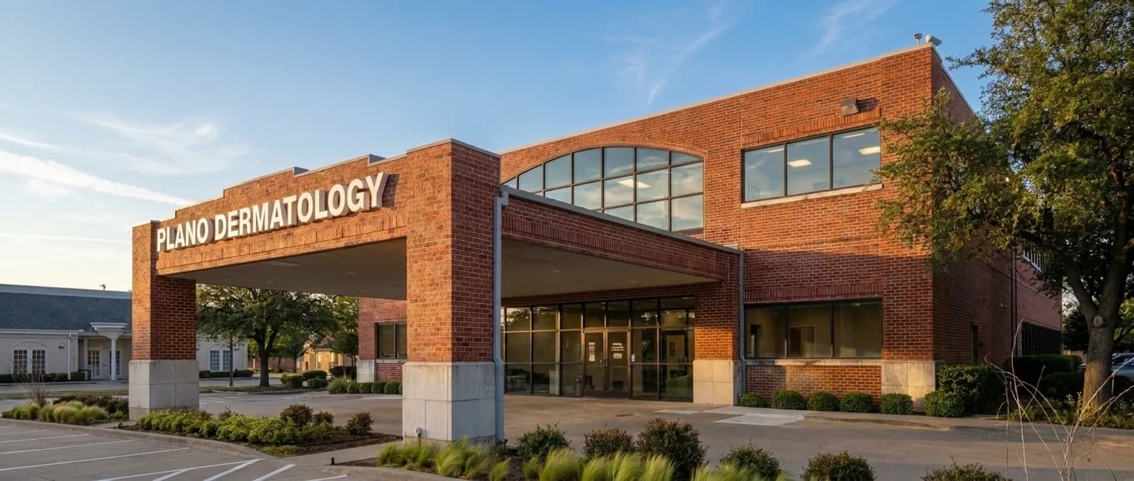 The Plano Dermatology building: two-story red brick with a drive-under porte-cochere and PLANO DERMATOLOGY in white letters