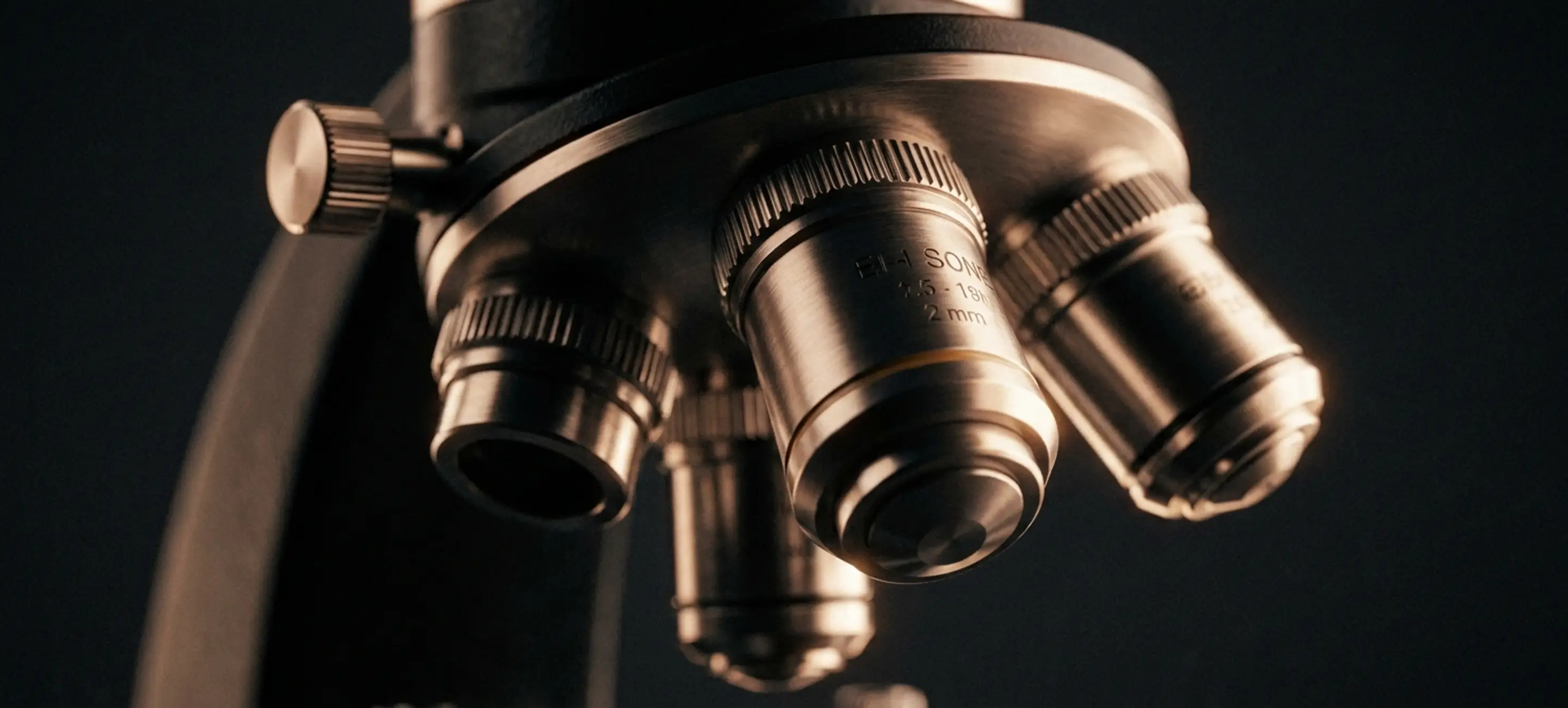 Macro detail of a bronze-rimmed microscope objective against a dark ground